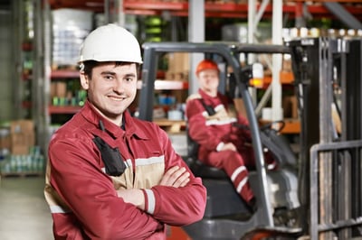 Smiling male industrial worker in front of a forklift in a warehouse