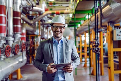 Smiling businessman in a factory with a tablet and hard hat