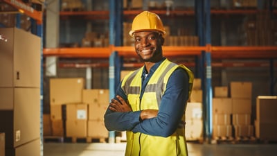 Smiling Black industrial worker wearing a hardhat and high vis vest in a warehouse