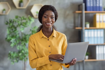 Smiling female procurer of color on a laptop with a yellow blouse