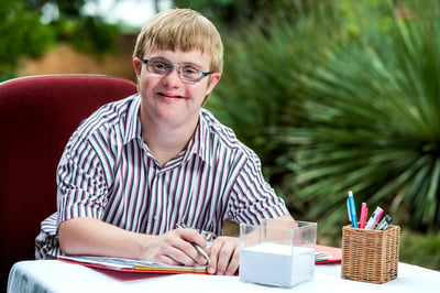 Smiling businessman with Down syndrome seated as a desk with a binder